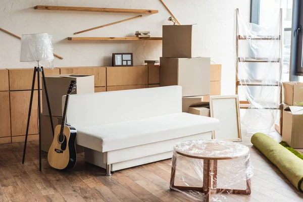 Cardboard boxes, rolled carpet, guitar and furniture in new apartment during relocation — Stock Photo