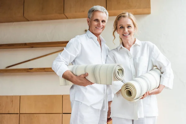 Feliz casal sênior segurando tapetes de ioga e sorrindo para a câmera — Fotografia de Stock