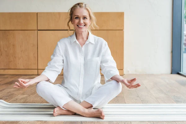 Happy mature woman sitting in lotus position and smiling at camera — Stock Photo