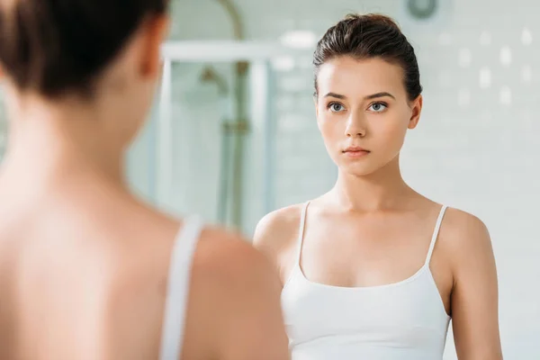 Красивая молодая женщина в нижнем белье смотрит в зеркало в ванной комнате — стоковое фото
