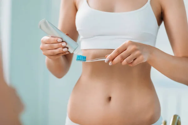 Visão parcial da menina em roupa interior segurando escova de dentes e pasta de dentes no banheiro — Fotografia de Stock