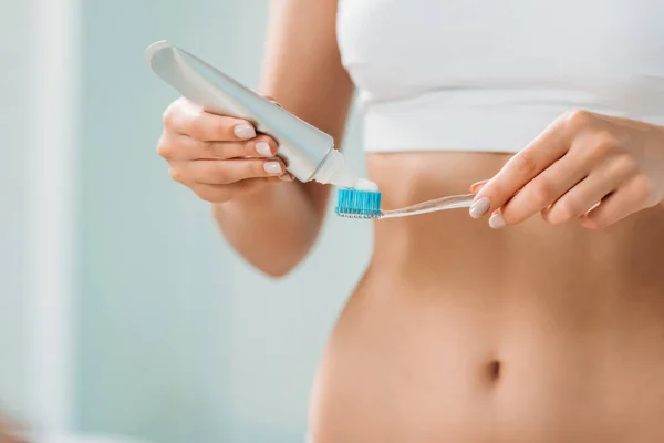 Corte tiro de jovem mulher em roupa interior segurando escova de dentes e pasta de dentes no banheiro — Fotografia de Stock