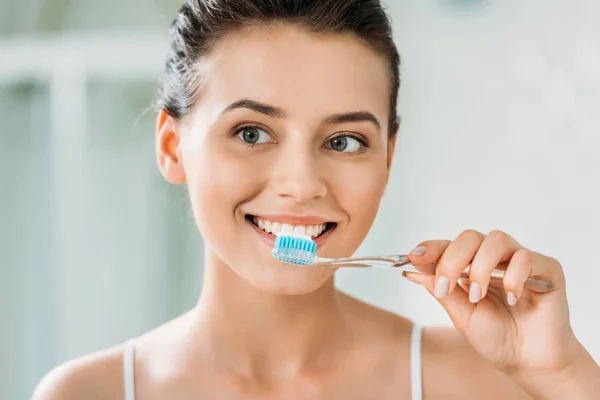 Hermosa chica sonriente cepillarse los dientes en el baño - foto de stock