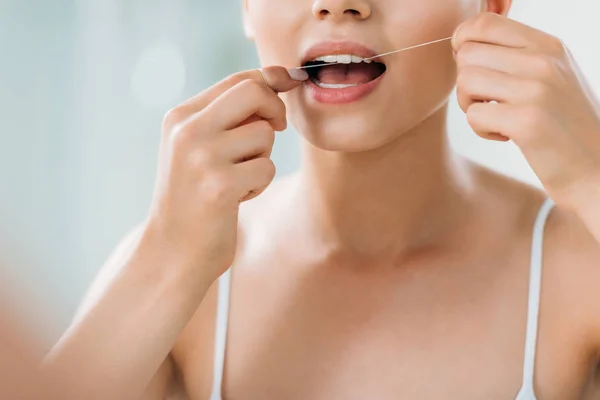 Tiro recortado de mujer joven usando hilo dental en el baño - foto de stock