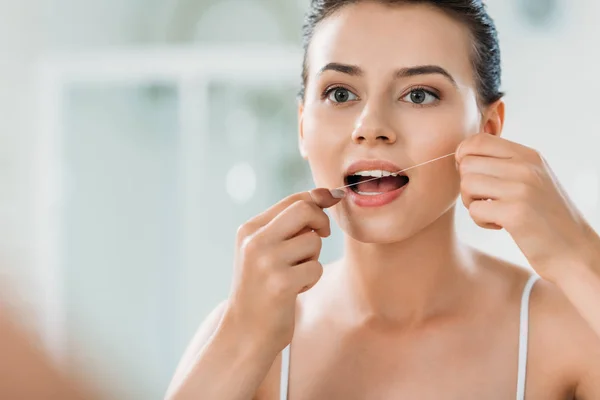 Schöne junge Frau mit Zahnseide im Badezimmer — Stockfoto