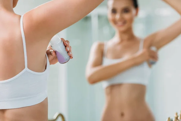 Selective focus of smiling girl applying roller deodorant at mirror in bathroom — Stock Photo