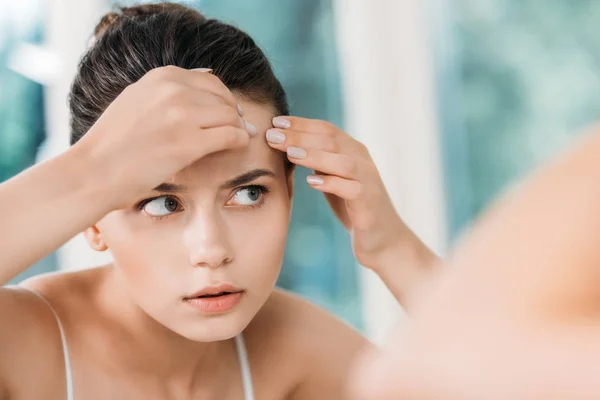 Селективное внимание девушки, проверяющей кожу на лбу и смотрящей на зеркало в ванной комнате — стоковое фото