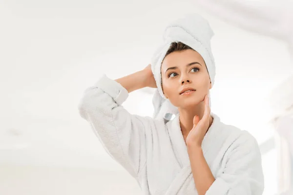 Vue à angle bas de belle fille coûteuse en peignoir et serviette sur la tête regardant loin dans la salle de bain — Photo de stock