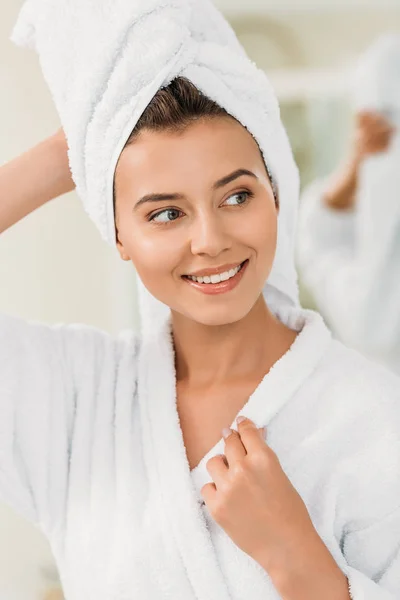 Красива усміхнена дівчина в халаті та рушнику на голові дивиться у ванну кімнату — стокове фото