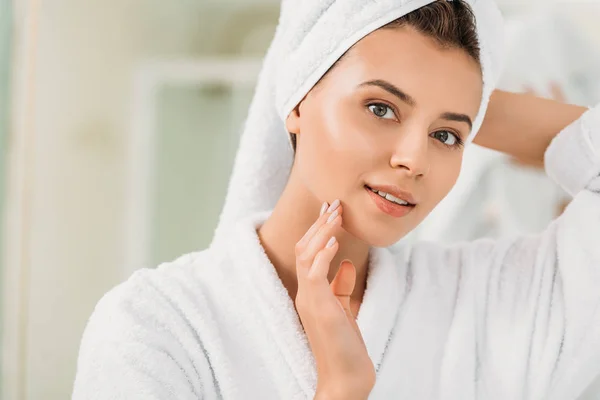 Beautiful smiling girl in bathrobe and towel on head looking at camera in bathroom — Stock Photo