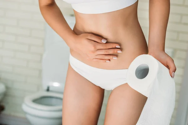 Vista parcial de la niña en ropa interior blanca sosteniendo papel higiénico mientras sufre de diarrea — Stock Photo