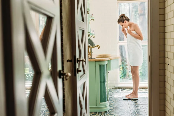 Vista lateral de la mujer joven de pie en balanzas digitales en el baño - foto de stock