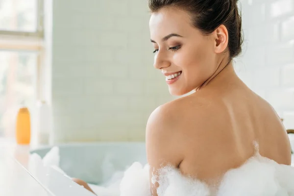 Bela menina nua sorridente sentado na banheira com espuma — Fotografia de Stock