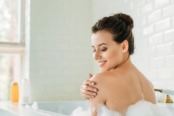 Hermosa mujer joven sonriente relajarse en la bañera con espuma - foto de stock