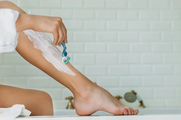 Обрезанный снимок молодой женщины, бреющей ноги бритвой в ванной комнате — стоковое фото