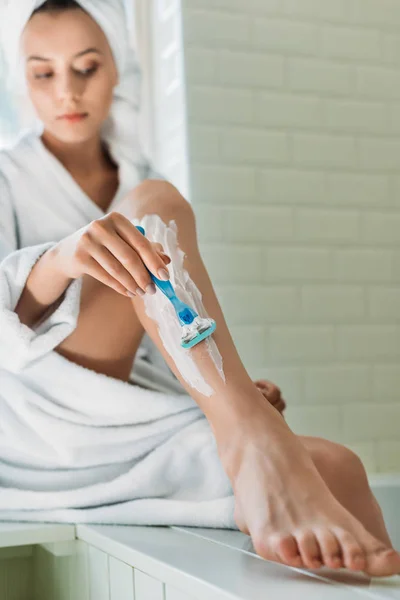 Mujer joven afeitarse la pierna con afeitadora en el baño - foto de stock