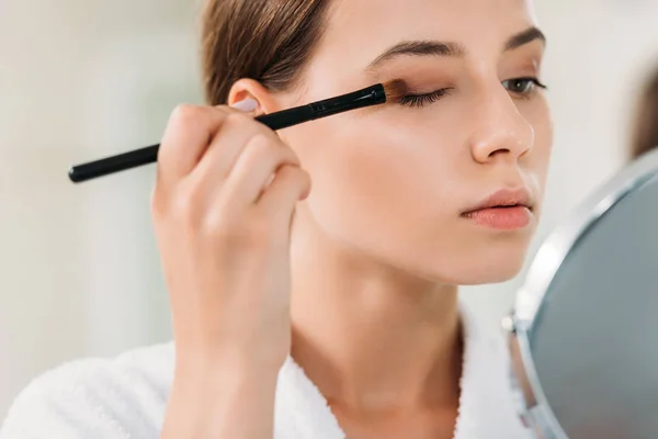 Close-up view of beautiful young woman applying eyeshadow with brush — Stock Photo