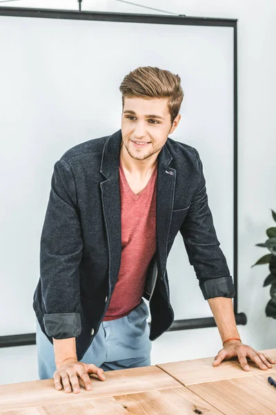 Retrato de joven hombre de negocios sonriente apoyado en la mesa en la oficina - foto de stock