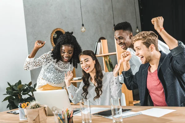 Multicultural group of business people celebrating success at workplace with laptop — Stock Photo