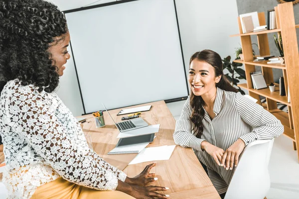 Multiethnic smiling businesswomen having conversation at workplace in office — Stock Photo