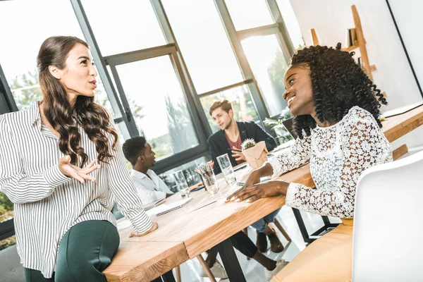 Multiethnic smiling businesswomen having conversation at workplace in office — Stock Photo