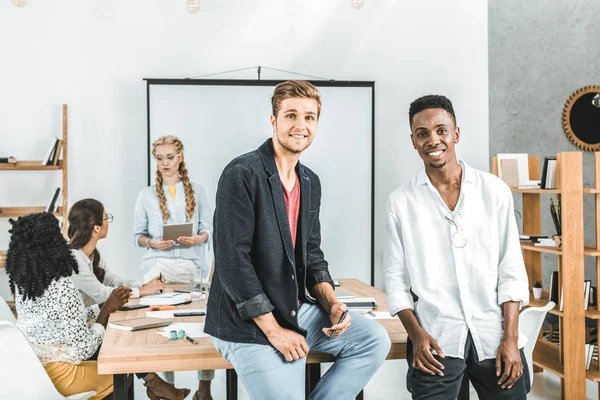 Multikulturell lächelnde Geschäftsleute blicken in die Kamera und Kollegen diskutieren die Arbeit hinter den Kulissen im Büro — Stockfoto