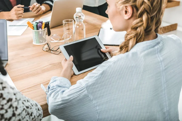 Vue latérale de la femme d'affaires tenant une tablette numérique alors qu'elle était assise à table lors d'une réunion avec ses collègues — Photo de stock