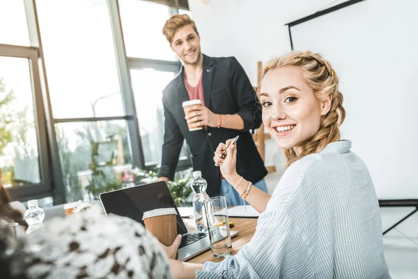 Seitenansicht einer lächelnden Geschäftsfrau mit Coffee to go am Tisch während eines Geschäftstreffens — Stockfoto