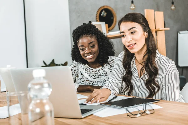 Portrait of beautiful asian and african american businesswomen working on laptop together at workplace — Stock Photo