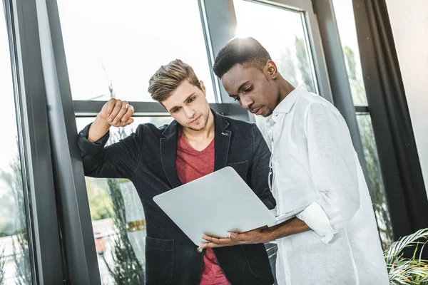 Uomini d'affari multiculturali fiduciosi che lavorano insieme sul computer portatile in ufficio — Foto stock