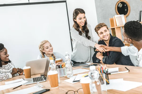 Smiling multiethnic business partners shaking hands during conference with multicultural colleagues in office — Stock Photo