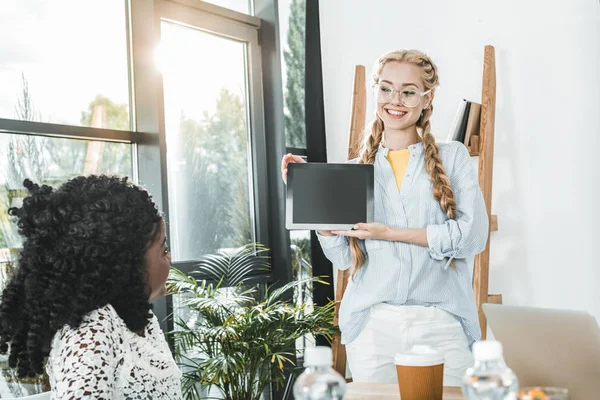 Porträt einer lächelnden kaukasischen Geschäftsfrau, die einem afrikanisch-amerikanischen Amtskollegen ein Tablet zeigt — Stockfoto