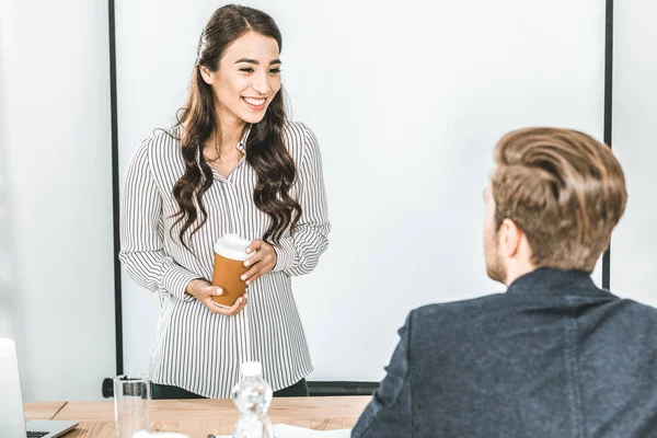 Portrait of smiling asian businesswoman with coffee to go talking with colleague in office — Stock Photo