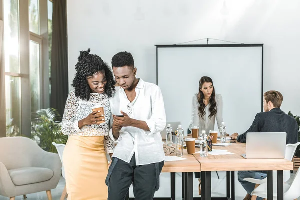 Sonrientes empresarios afroamericanos usando un smartphone juntos en la oficina - foto de stock