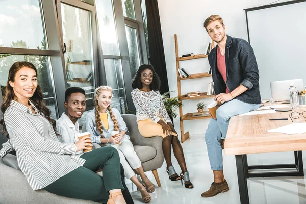 Compañeros de trabajo sonrientes multiétnicos mirando a la cámara mientras toma un descanso de café en la oficina - foto de stock