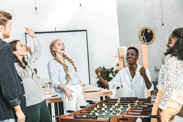 Happy multicultural colleagues celebration win while playing table football in office — Stock Photo