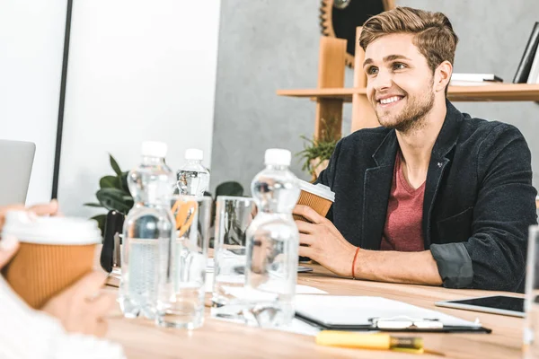 Retrato de um jovem empresário sorridente sentado à mesa durante a reunião no cargo — Fotografia de Stock