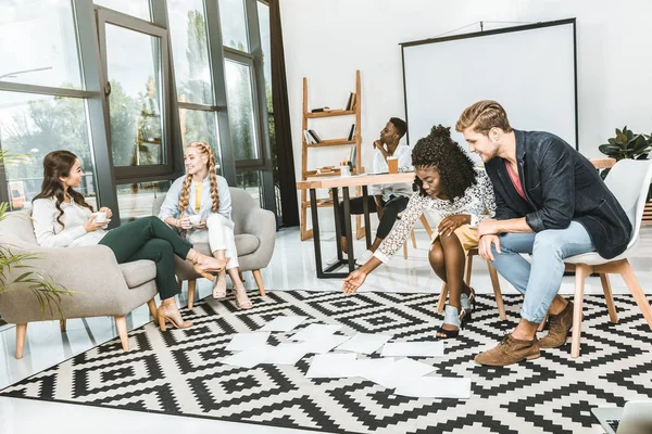 Multicultural business people looking at papers on floor together in office — Stock Photo