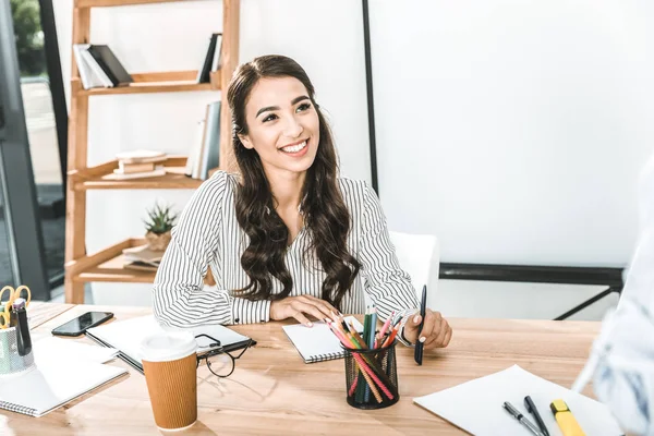 Retrato de sonriente asiático mujer de negocios sentado en el lugar de trabajo con varios suministros de oficina - foto de stock