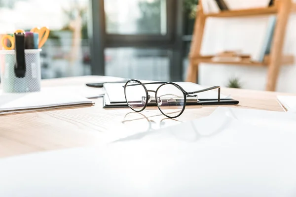 Selective focus of round eyeglasses on workplace with papers and clipboard — Stock Photo
