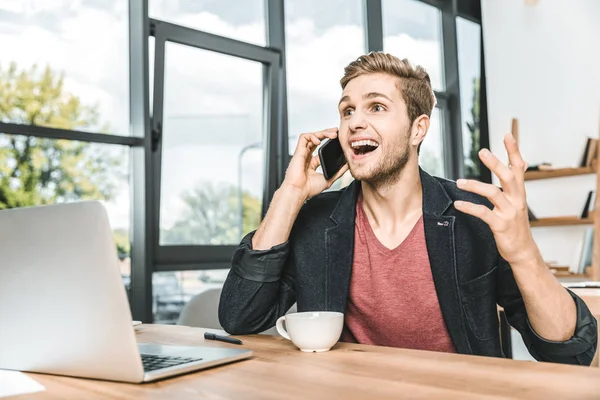 Porträt eines aufgeregten Geschäftsmannes, der am Arbeitsplatz im Büro mit dem Smartphone spricht — Stockfoto