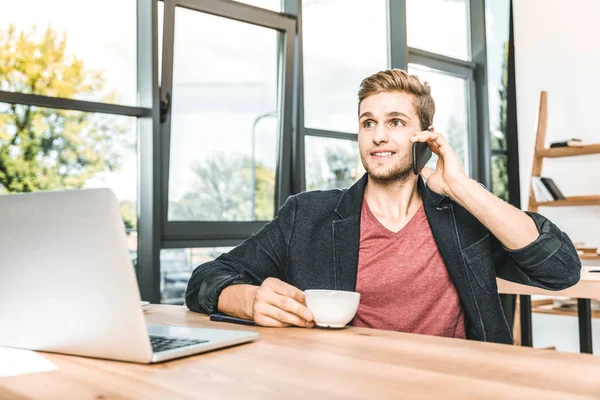 Porträt eines jungen Geschäftsmannes, der am Arbeitsplatz im Büro mit dem Smartphone spricht — Stockfoto