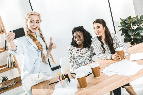 Multicultural smiling businesswomen taking selfie on smartphone at workplace — Stock Photo