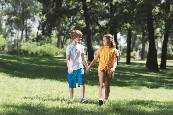 Beautiful happy children holding hands and walking together in park — Stock Photo