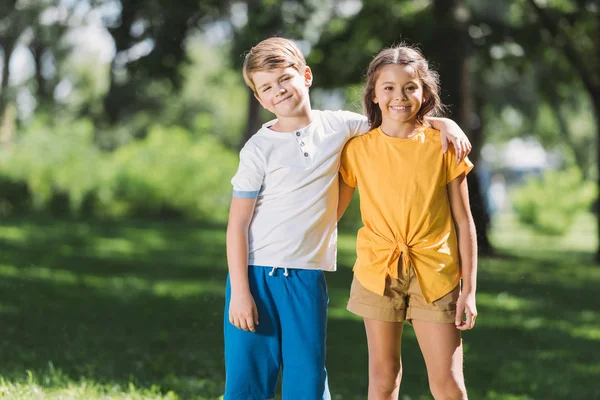 Hermosos niños felices abrazando y sonriendo a la cámara en el parque - foto de stock