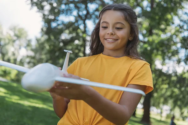 Крупный план симпатичного улыбающегося ребенка, держащего в руках модель игрушечного самолета в парке — стоковое фото