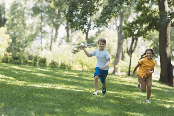 Simpatici bambini felici che giocano con il modello aereo e corrono nel parco — Foto stock