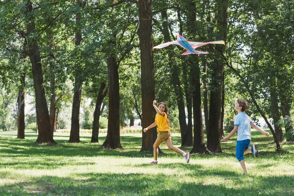 Lindo feliz niños jugando con colorido cometa en parque - foto de stock