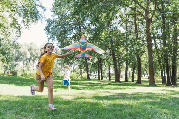 Adorable feliz niños jugando con colorido cometa en parque - foto de stock