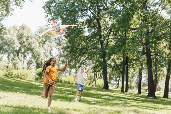 Lindo feliz niños jugando con colorido cometa en parque - foto de stock